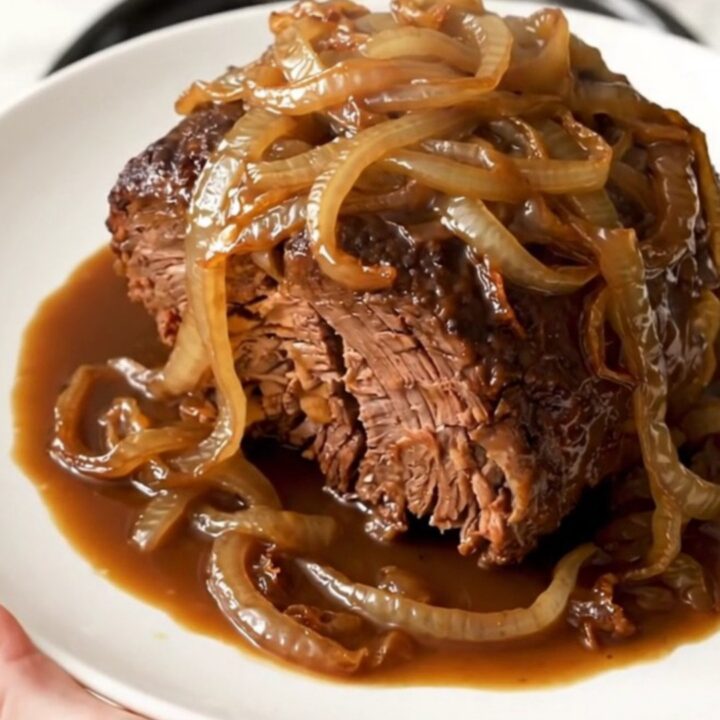 A close-up of a tender, slow-cooked beef roast served on a white plate with caramelized onions.