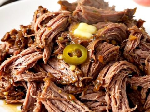 A close-up of tender, shredded Mississippi Pot Roast on a white plate with pepperoncini peppers.