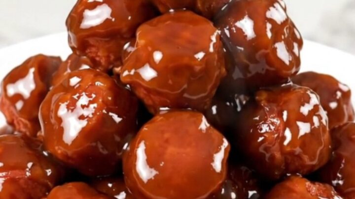 A close-up shot of glossy, glazed kielbasa bites in a slow cooker on a white quartz countertop.