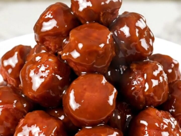 A close-up shot of glossy, glazed kielbasa bites in a slow cooker on a white quartz countertop.