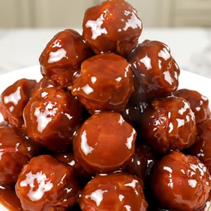 A close-up shot of glossy, glazed kielbasa bites in a slow cooker on a white quartz countertop.