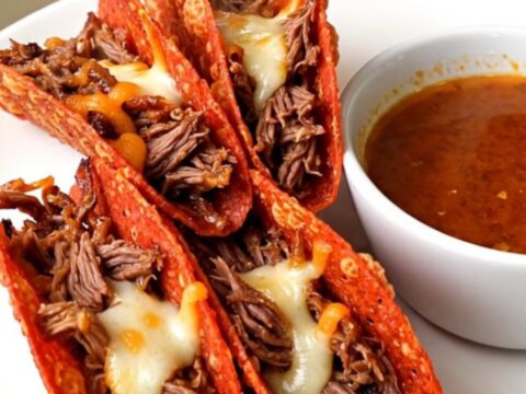 A close-up of crispy, golden-brown beef birria tacos served on a white plate with a side of savory dipping broth.