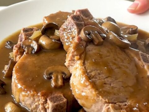 Close up of tender pork chops covered in creamy mushroom gravy on a white plate.