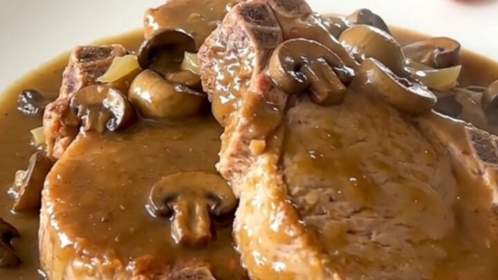 Close up of tender pork chops covered in creamy mushroom gravy on a white plate.