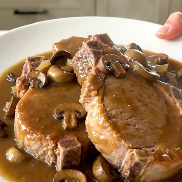 Close up of tender pork chops covered in creamy mushroom gravy on a white plate.