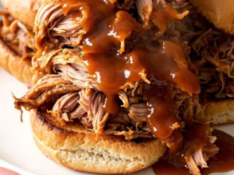 A close-up view of steaming pumpkin barbecue pulled pork piled high on toasted pretzel slider buns.