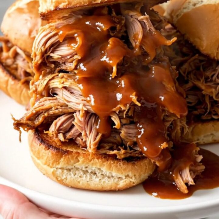 A close-up view of steaming pumpkin barbecue pulled pork piled high on toasted pretzel slider buns.