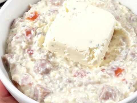 A steaming bowl of creamy white sausage queso dip in a white bowl with tortilla chips nearby.