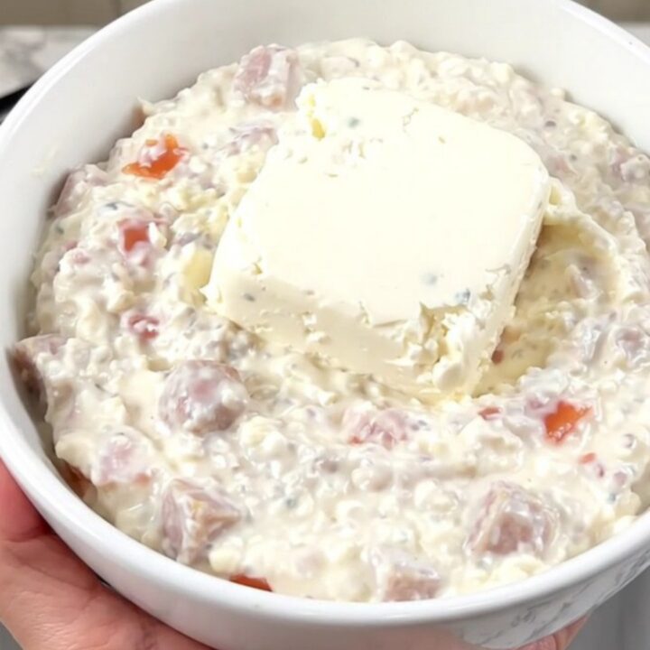 A steaming bowl of creamy white sausage queso dip in a white bowl with tortilla chips nearby.