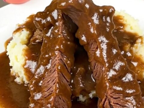 A close-up shot of tender beef tips and rich brown mushroom gravy served over creamy mashed potatoes.