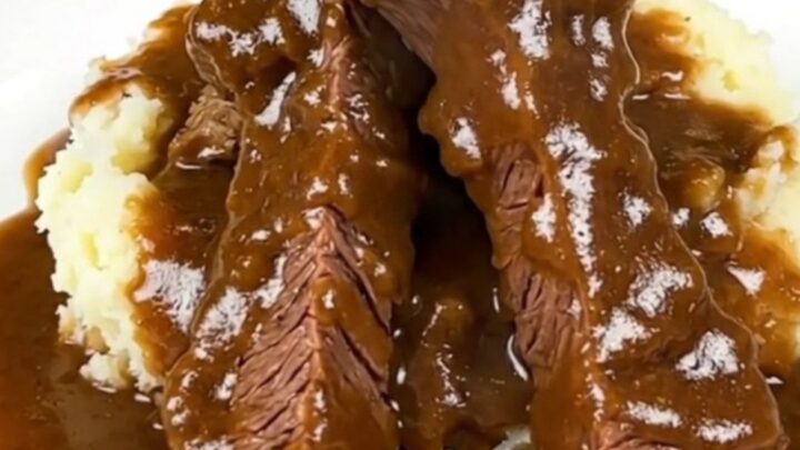 A close-up shot of tender beef tips and rich brown mushroom gravy served over creamy mashed potatoes.