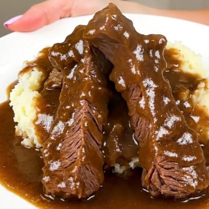 A close-up shot of tender beef tips and rich brown mushroom gravy served over creamy mashed potatoes.
