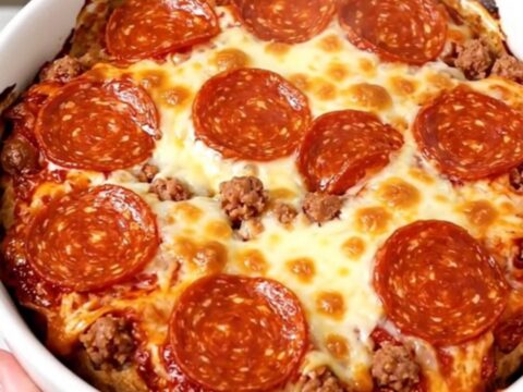A top-down view of a black slow cooker filled with layers of cream cheese, sausage, mozzarella, and pepperoni before cooking.