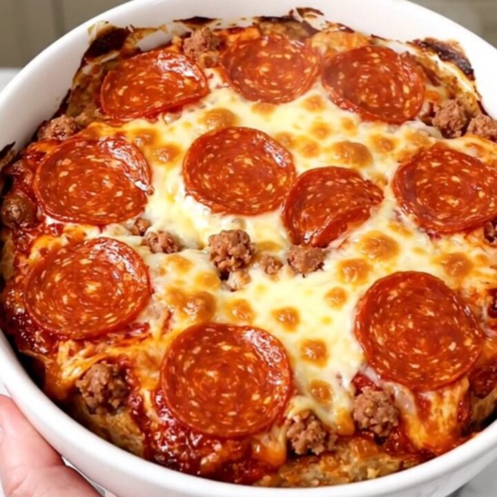A top-down view of a black slow cooker filled with layers of cream cheese, sausage, mozzarella, and pepperoni before cooking.