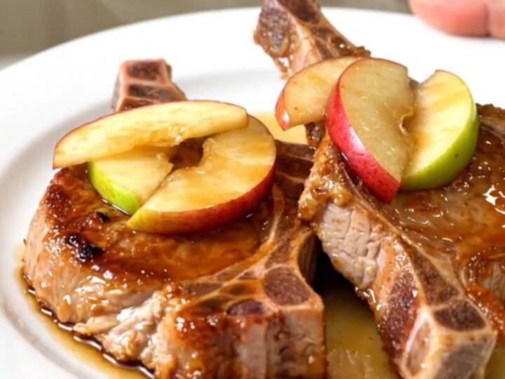 A close-up of glossy, cooked pork chops topped with tender caramelized apples on a white plate.