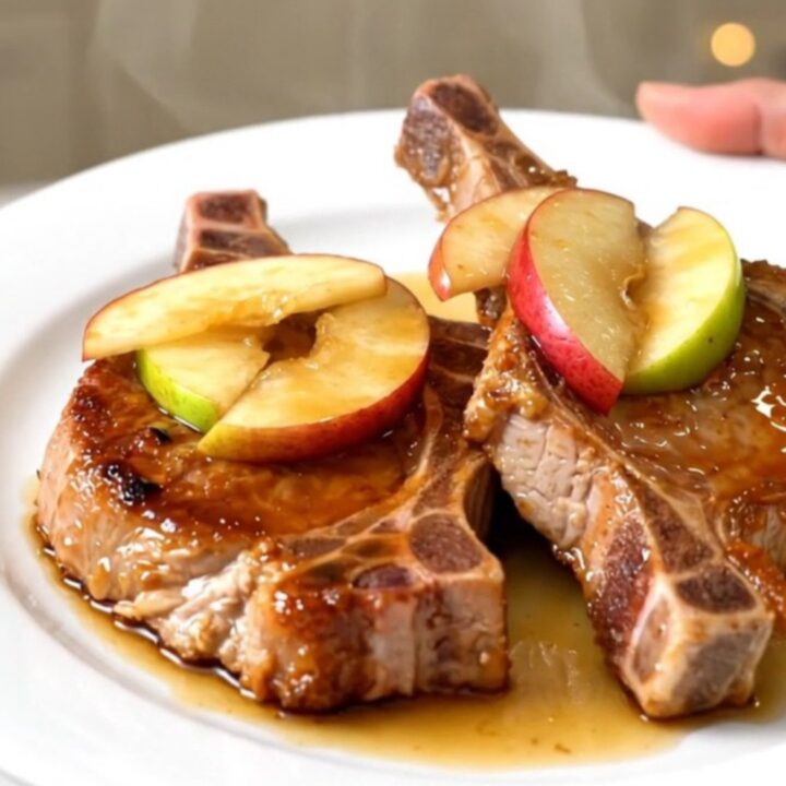 A close-up of glossy, cooked pork chops topped with tender caramelized apples on a white plate.