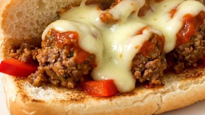 A steaming, toasted hoagie roll filled with meatballs, peppers, and melted provolone cheese on a white plate.