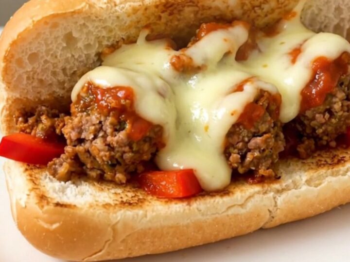 A steaming, toasted hoagie roll filled with meatballs, peppers, and melted provolone cheese on a white plate.