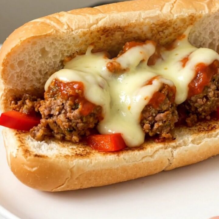 A steaming, toasted hoagie roll filled with meatballs, peppers, and melted provolone cheese on a white plate.