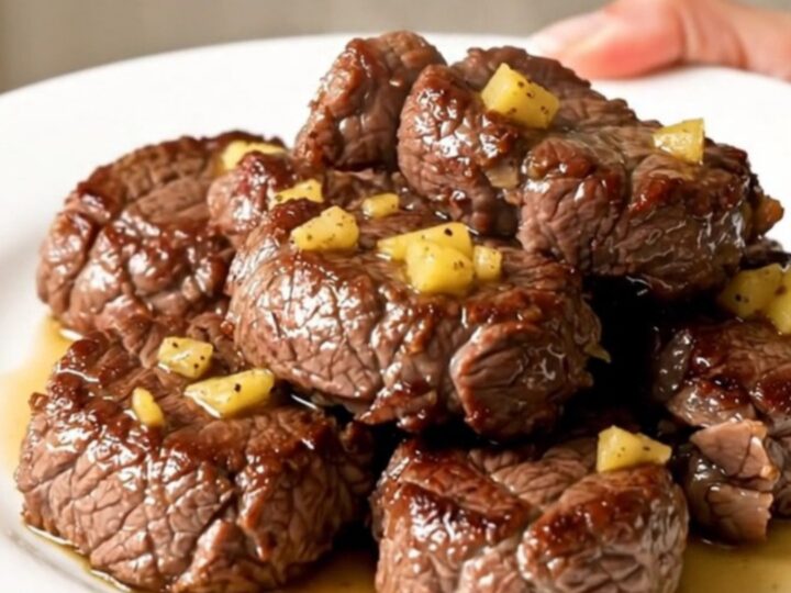 A top-down view of raw steak cubes, butter, and seasonings inside a black slow cooker bowl.