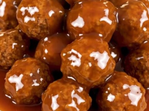 A close-up of glossy, glazed sweet and sour meatballs in a slow cooker.
