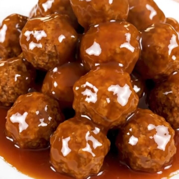 A close-up of glossy, glazed sweet and sour meatballs in a slow cooker.