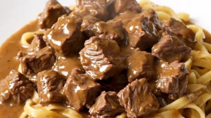 A top-down view of a black slow cooker filled with raw beef stew meat and mushrooms ready for cooking.