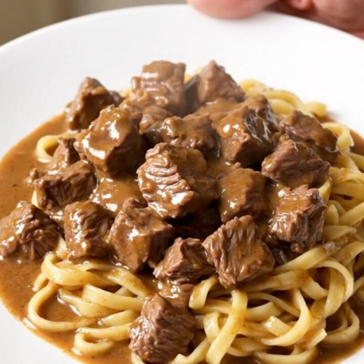 A top-down view of a black slow cooker filled with raw beef stew meat and mushrooms ready for cooking.