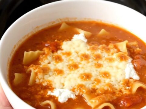 A steaming, glossy bowl of lasagna soup topped with melted mozzarella cheese on a kitchen counter.