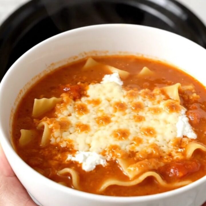 A steaming, glossy bowl of lasagna soup topped with melted mozzarella cheese on a kitchen counter.