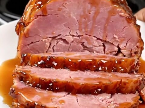 A succulent, glazed boneless ham sitting in a black slow cooker on a white speckled countertop.