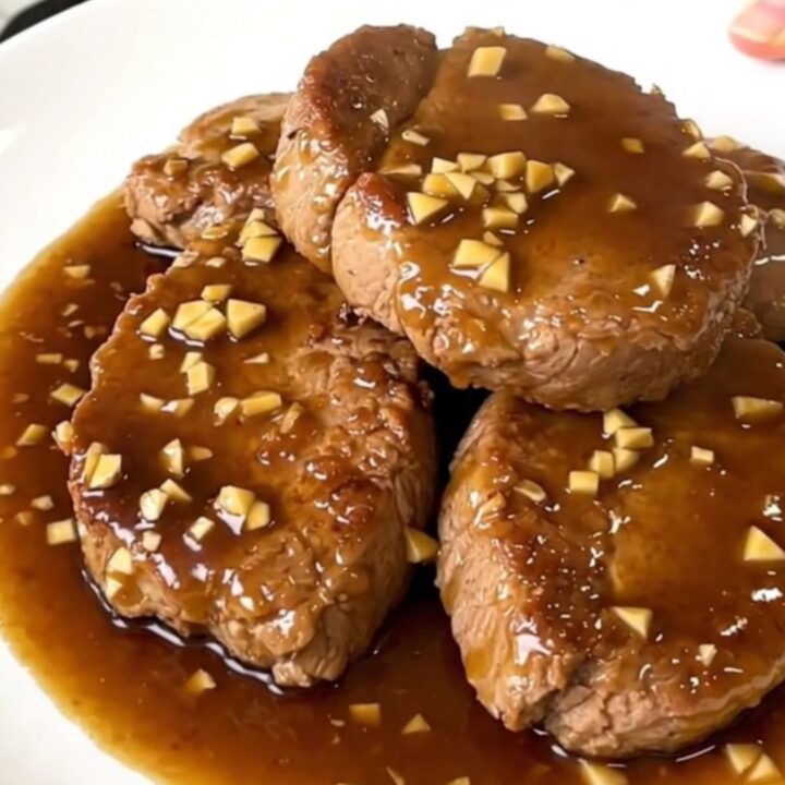 A slow cooker filled with raw pork tenderloins and sauce ingredients on a white speckled countertop.