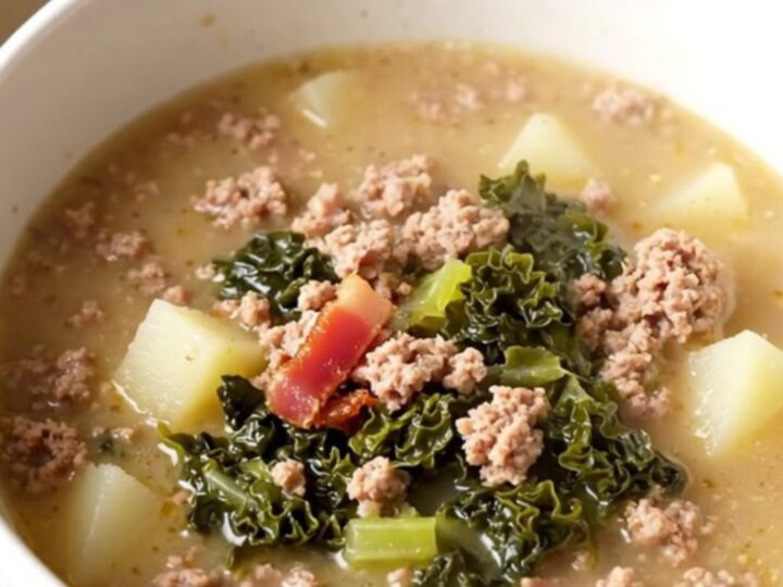 A steaming bowl of Zuppa Toscana filled with sausage, potatoes, and kale on a white background.