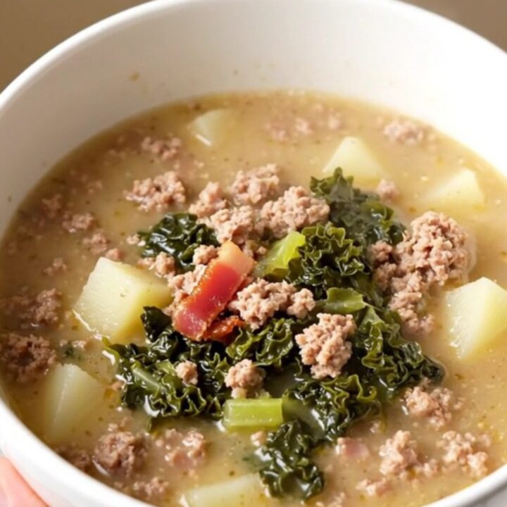 A steaming bowl of Zuppa Toscana filled with sausage, potatoes, and kale on a white background.