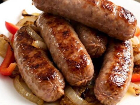 A slow cooker filled with cooked bratwurst, sliced bell peppers, and onions in a beer-based sauce.