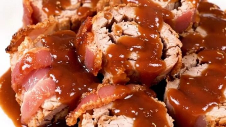 A close-up of slow-cooked bacon-wrapped pork tenderloin slices arranged on a white plate.