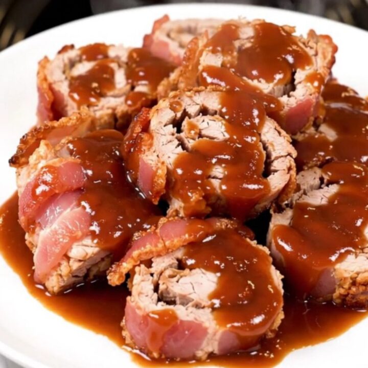 A close-up of slow-cooked bacon-wrapped pork tenderloin slices arranged on a white plate.