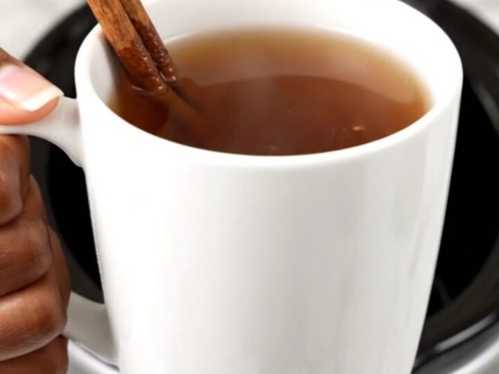 A slow cooker filled with hot apple cider, sliced oranges, and spices on a white countertop.
