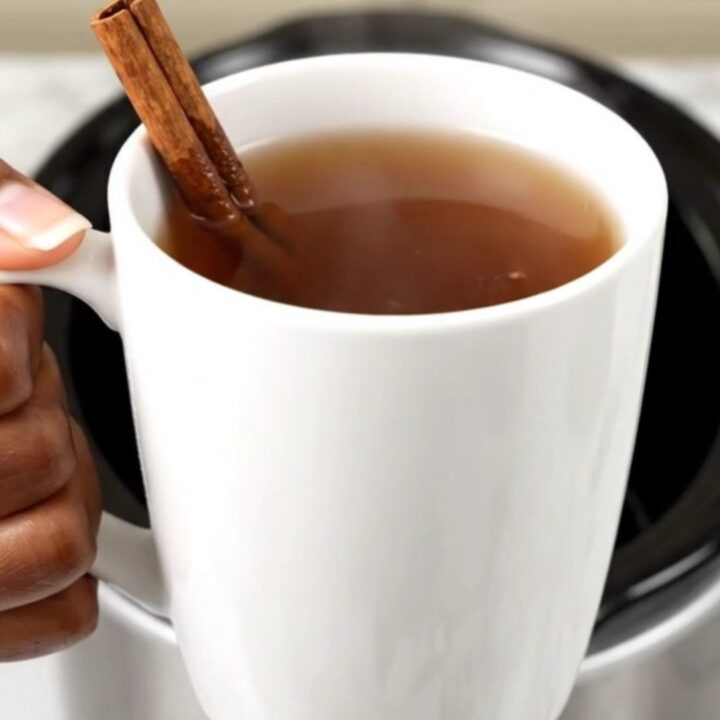 A slow cooker filled with hot apple cider, sliced oranges, and spices on a white countertop.