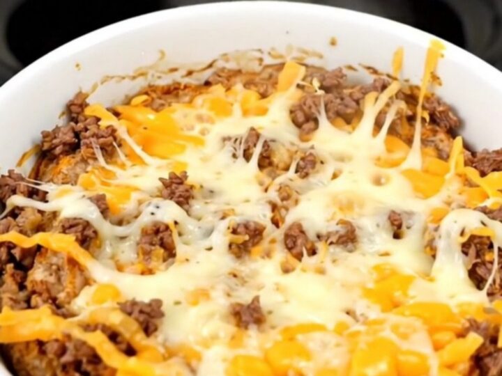 A warm, bubbling bowl of beef enchilada dip in a slow cooker.
