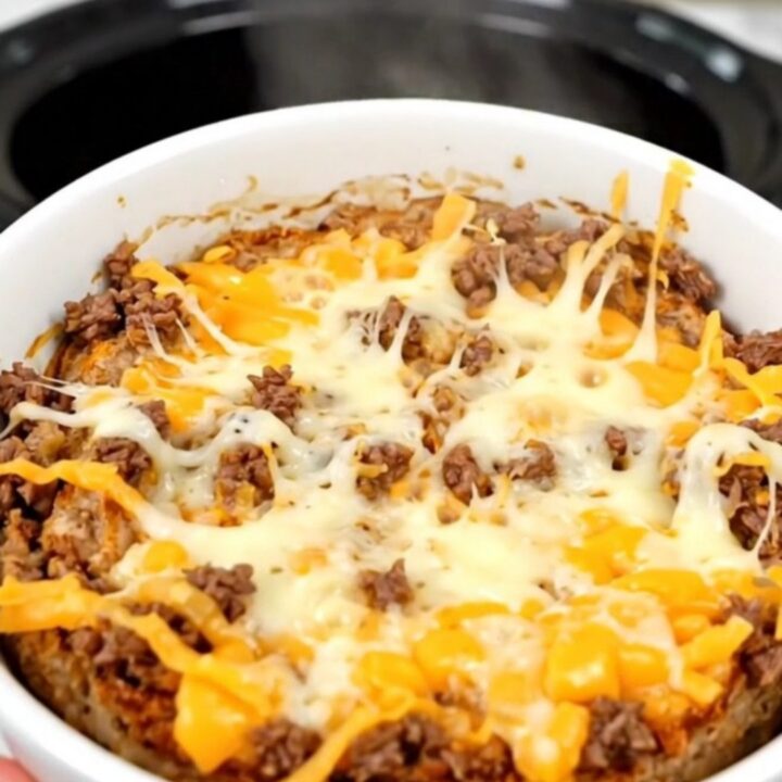 A warm, bubbling bowl of beef enchilada dip in a slow cooker.