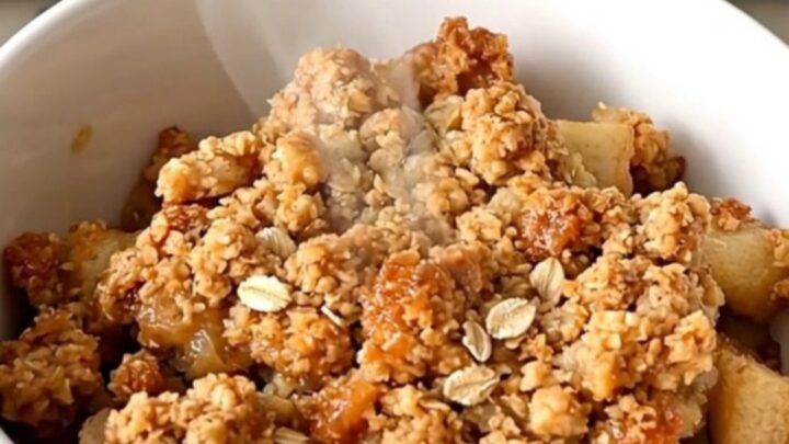 A warm, golden-brown apple crisp in a slow cooker with visible apple slices and a crunchy oat topping.