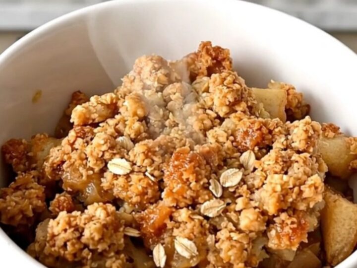 A warm, golden-brown apple crisp in a slow cooker with visible apple slices and a crunchy oat topping.