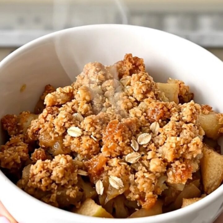 A warm, golden-brown apple crisp in a slow cooker with visible apple slices and a crunchy oat topping.