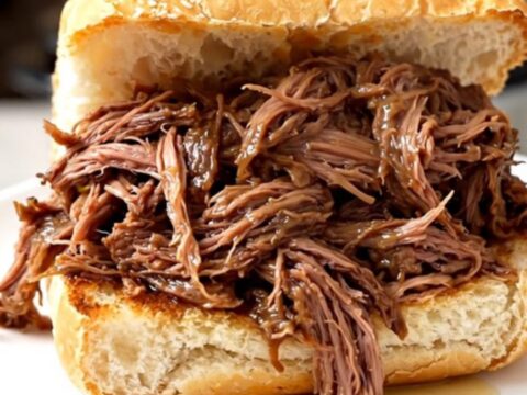 A steaming, juicy Italian beef sandwich on a crusty roll held on a white plate.