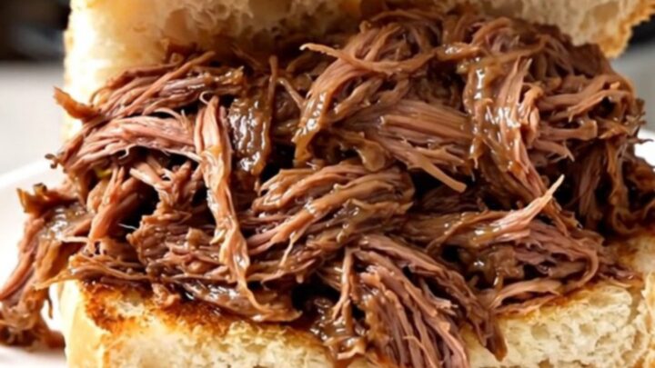 A steaming, juicy Italian beef sandwich on a crusty roll held on a white plate.