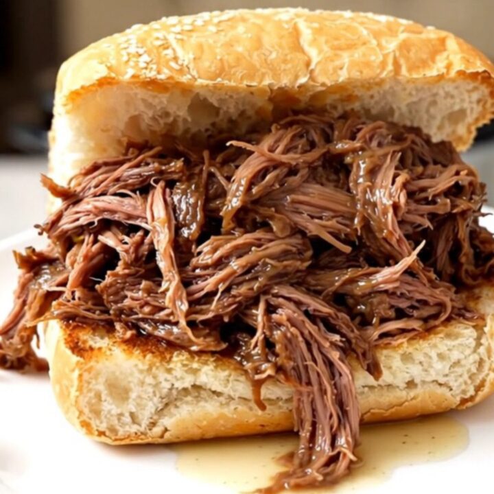 A steaming, juicy Italian beef sandwich on a crusty roll held on a white plate.