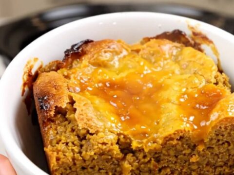 A warm, steaming pumpkin dump cake served in a white bowl against a blurred kitchen background.