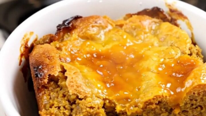 A warm, steaming pumpkin dump cake served in a white bowl against a blurred kitchen background.