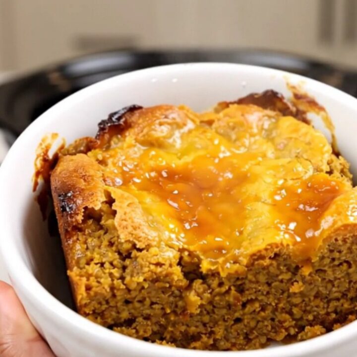 A warm, steaming pumpkin dump cake served in a white bowl against a blurred kitchen background.